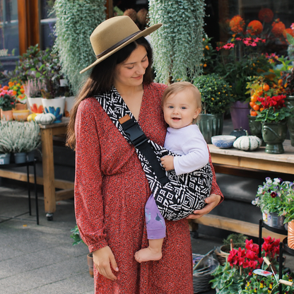 Woman holding a baby in a sling amidst a flower shop setting